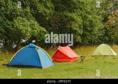 Trois tentes de camping stables de différentes couleurs, bleu, rouge et vert clair, installées sur l'herbe devant les arbres à feuillage, promettant une aventure inoubliable Banque D'Images