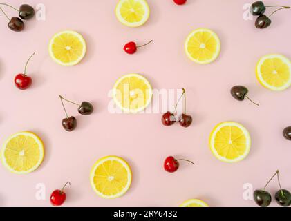 Motif de fruits créatifs fait de cerises rouges et de tranches de citron jaune sur fond rose pastel clair. Disposition minimale de cerises naturelles et d'agrumes. Banque D'Images