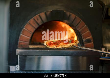 Pizza rouge émergeant du four à bois Banque D'Images