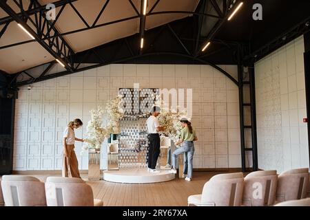 équipe créative de concepteurs d'événements préparant une salle de fête moderne en arrangeant la composition florale Banque D'Images