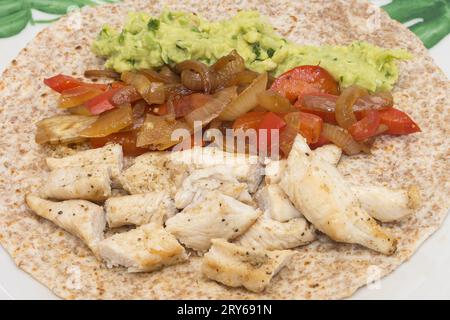 Gros plan d'une tortilla fajita au poulet de blé entier avec poulet assaisonné au cumin, guacamole maison et mélange croquant d'oignon semi-cru et rouge Banque D'Images