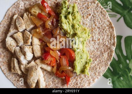 Vue aérienne d'une tortilla ouverte au poulet de blé entier Fajita servie sur une assiette avec succulent poulet assaisonné, légumes vibrants et guacamole. Banque D'Images