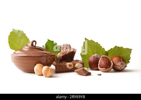 Chocolat aux noisettes et crème dans un bol en verre avec noix et feuilles isolées sur blanc. Vue avant. Banque D'Images