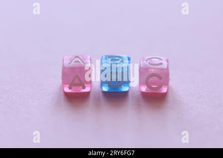 macro shot de perles roses et bleues épelant abc sur un fond rose Banque D'Images