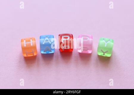perles colorées épelant le mot heureux sur un fond rose Banque D'Images
