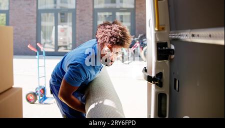 Jeune homme Movers chargement du tapis roulé vers le camion sur la rue Banque D'Images