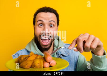 Portrait de personne impressionnée surjoyée ouverte bouche tenir la fourchette délicieuse assiette de saucisses de pommes de terre frites isolée sur fond jaune Banque D'Images