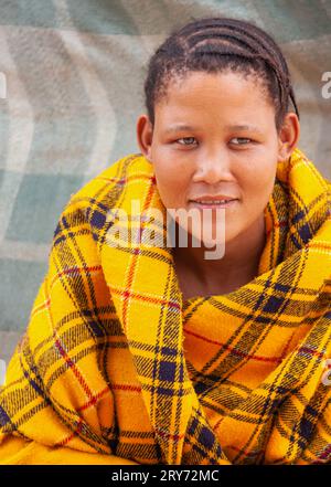 Un jeune bushmen san Woman du Kalahari central, village de New Xade au Botswana, enveloppé sur une couverture jaune dans la cour de la maison après son déménagement Banque D'Images