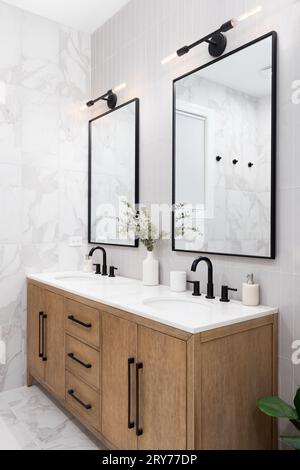 Une salle de bains avec des carreaux de métro verticaux en marbre et empilés, un meuble-lavabo en chêne blanc, des miroirs carrés encadrés de noir et des robinets, et un comptoir en marbre. Banque D'Images