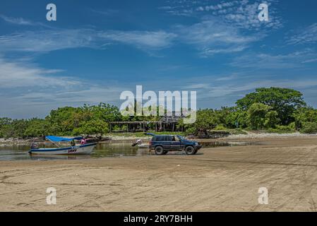 Zihuatanejo, Mexique - 18 juillet 2023 : tirer un petit bateau à moteur de pêche Lucky sur Playa Larga sablonneux avec l'aide d'un camion sous un paysage nuageux bleu. Folia verte Banque D'Images