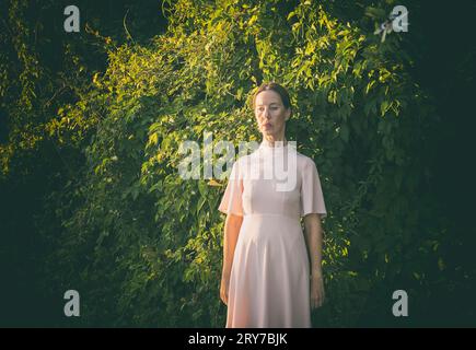 Femme en robe rose courte devant une haie V Banque D'Images