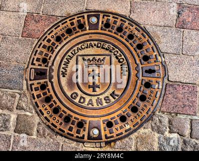 Couvercle de trou d'homme de la ville Gdansk armoiries symbole long main Square Gdansk Pologne. Le symbole date de 1457. Couronne au-dessus de deux croix. La langue polonaise ci-dessus disent Banque D'Images