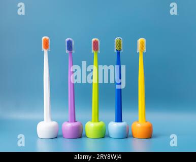 Grand nombre de brosses à dents de couleur vive sur les supports, support dans la rangée sur fond bleu. Hygiène matinale, Accessoires de salle de bain. Soins dentaires Banque D'Images