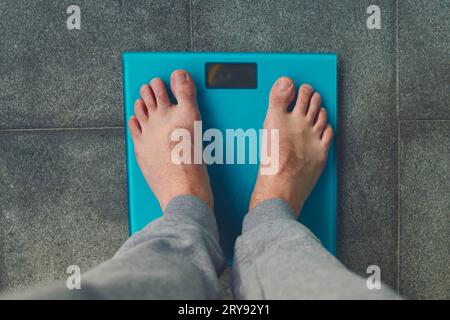 Homme debout sur une balance. Pieds mâles sur des balances en verre, régime pour hommes, poids corporel, gros plan, homme monter sur des balances, vue latérale Banque D'Images