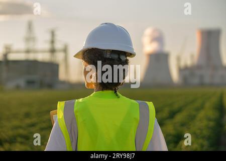 Vue arrière du constructeur d'ingénieur féminin se tient sur le terrain sur le fond d'entreprise industrielle Banque D'Images