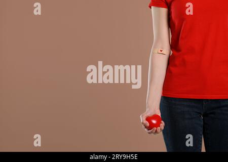 Concept de don de sang. Femme avec le plâtre adhésif sur le bras tenant le coeur rouge sur fond brun, closeup. Espace pour le texte Banque D'Images