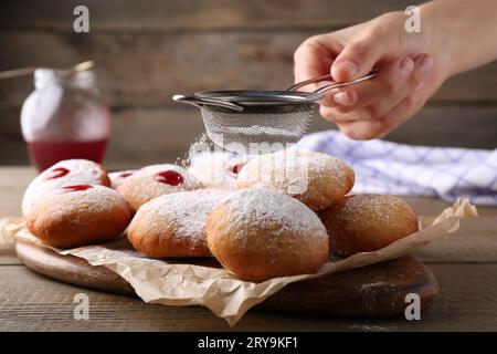 Femme saupoudrant le sucre en poudre sur de délicieux beignets Hanukkah sur la table en bois, gros plan Banque D'Images