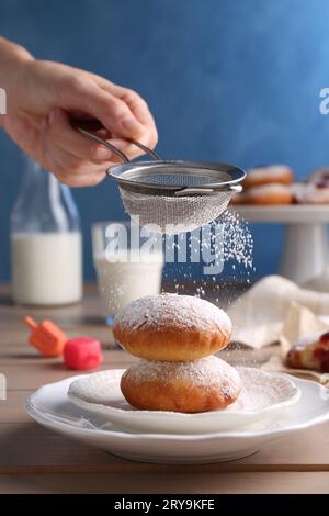 Femme saupoudrant le sucre en poudre sur de délicieux beignets Hanukkah sur la table en bois, gros plan Banque D'Images