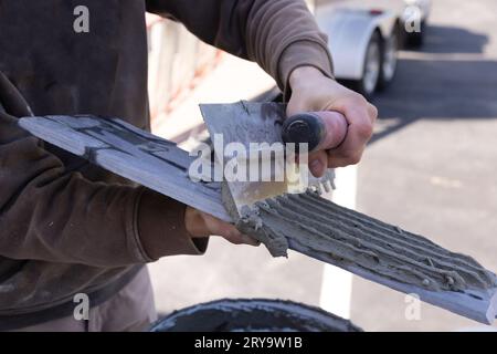 Avant d'appliquer les carreaux, l'homme étale l'adhésif de ciment humide avec des truelles Banque D'Images