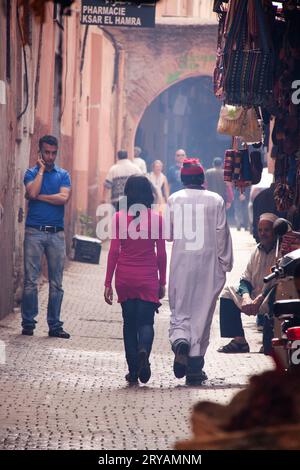 Fille locale et homme en robe blanche traditionnelle marchent à travers le souk de rue arrière muré à Marrakech Maroc Mars 2012 Banque D'Images