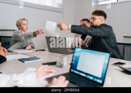 Vue à distance à un chef d'équipe féminin d'âge moyen qui distribue des documents contenant les résultats d'études marketing à des collègues lors d'une réunion de brainstorming au bureau Banque D'Images