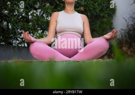 jeune belle femme enceinte médite assise sur un tapis de yoga sur une pelouse verte. concept de relaxation et de mode de vie sain Banque D'Images