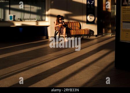 Femme assise sur un banc profitant du soleil chaud de l'après-midi, London Bridge Station, Londres, Royaume-Uni Banque D'Images