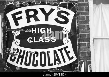 Un panneau publicitaire en métal vintage noir et blanc affiché sur un mur de briques Fry's chocolat, décrit sur l'annonce comme de grande classe Banque D'Images