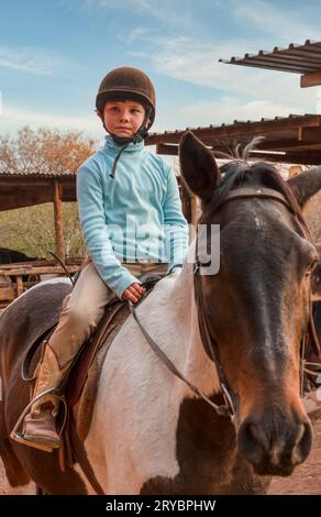 Fille avec un chapeau de cavaliers monté sur un cheval pinto, prenant des leçons d'équitation dans une écurie au Texas Banque D'Images