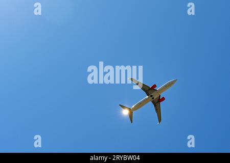 Jet de passagers moderne en vol isolé contre un ciel bleu avec le soleil brillant à la queue de l'avion. Concept de voyage Banque D'Images