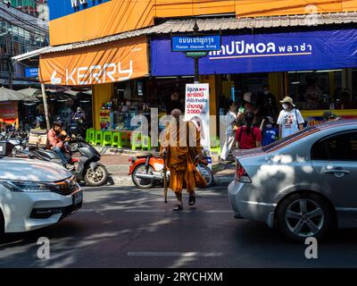 Un moine bouddhiste, vêtu de la robe traditionnelle au safran orange et portant un masque facial, traverse une rue de Bangkok, en Thaïlande. Banque D'Images