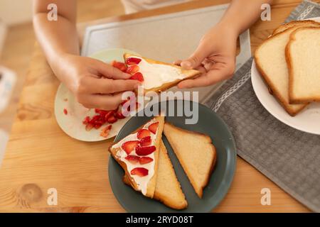 vue de dessus, une femme étale de la crème sure sur des toasts et met des fraises dessus Banque D'Images