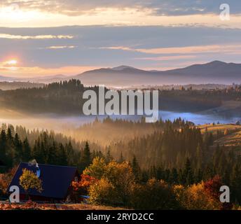 L'air. Tôt le matin, le brouillard et les premiers rayons de soleil du matin sur l'automne des pentes de montagnes des Carpates et méconnaissable farmstead (Ukraine). Banque D'Images