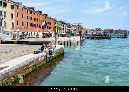 Venise, Italie - Mai 30 2023 : touristes assis au bord de l'eau et profitant de la scène idyllique sur le Grand Canal à Venise. Banque D'Images