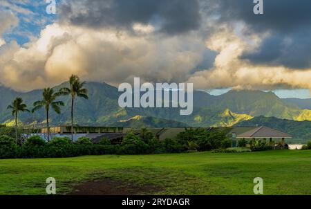 Le lever du soleil illumine les nuages d'orage au-dessus des montagnes Hanalei avec les bâtiments couverts de plantes du 1 Hôtel au premier plan Banque D'Images