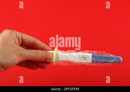 Close up woman hand holding test de grossesse avec condom sur fond rouge avec copie espace, low angle view Banque D'Images