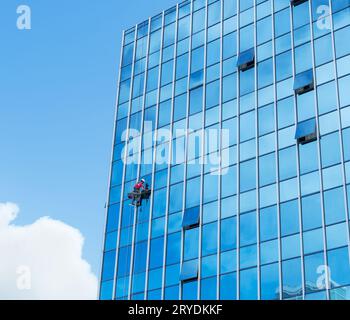 Nettoyant à travailler sur une façade de verre suspendue Banque D'Images