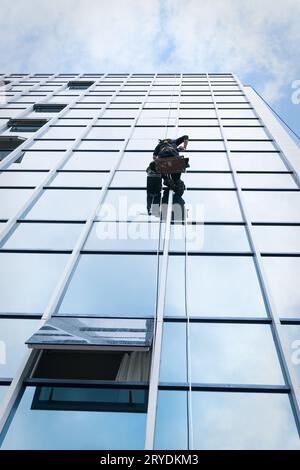 Nettoyant à travailler sur une façade de verre suspendue Banque D'Images