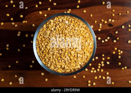 Un bol en verre de pois chiches daal-pigeon jaunes éparpillés sur une table en bois Banque D'Images