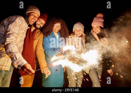 Groupe de personnes heureuses ayant des feux d'artifice partie à la célébration de nuit d'hiver avec des étincelles. Multiracial Banque D'Images