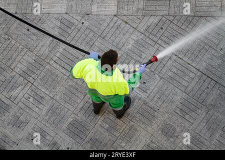 Travailleur tenant un tuyau pour nettoyer le trottoir avec de l'eau Banque D'Images