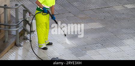 Travailleur nettoyant un trottoir de rue avec un jet d'eau à haute pression Banque D'Images