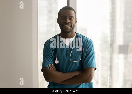 Heureux beau chirurgien afro-américain dans les gommages bleus debout à l'intérieur Banque D'Images