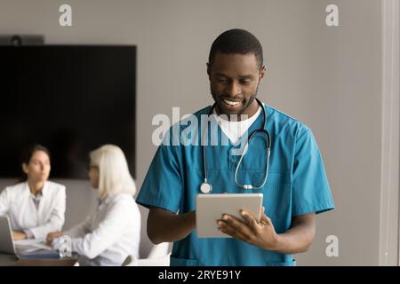 Jeune médecin africain positif utilisant le service médical Internet sur tablette Banque D'Images