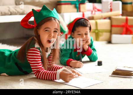 Mignons petits enfants habillés comme des elfes écrivant des lettres au Père Noël à la maison la veille de Noël Banque D'Images