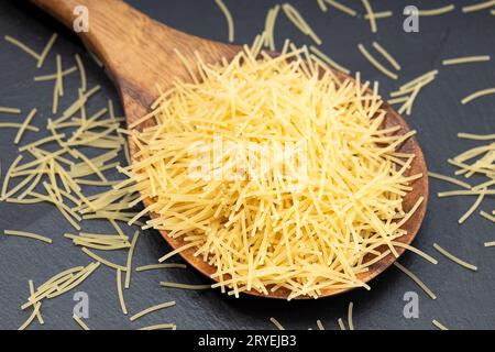 Pâtes de nouilles à soupe non cuites dans une cuillère en bois Banque D'Images