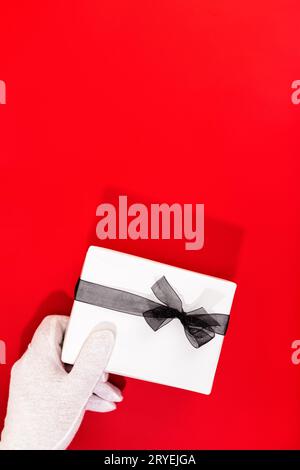 Père Noël avec des mains gantées tenant un cadeau de Noël sur fond rouge Banque D'Images