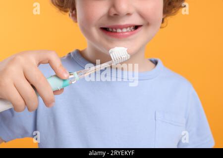 Mignon petit garçon tenant une brosse à dents électrique avec de la pâte sur fond jaune, gros plan Banque D'Images