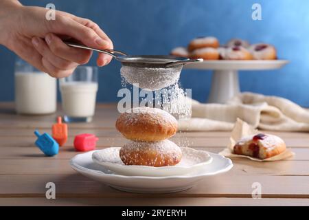 Femme saupoudrant le sucre en poudre sur de délicieux beignets Hanukkah sur la table en bois, gros plan Banque D'Images