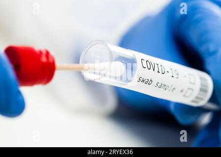 Test de diagnostic de la maladie virale RT-PCR COVID-19, technicien de laboratoire britannique portant un gant de protection bleu tenant le tube à essai avec tampon St Banque D'Images